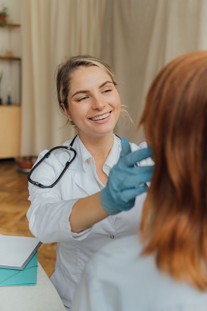 A doctor wearing disposable gloves examining a patients neck by feeling it with their hands